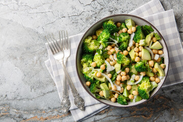 close-up of a dietary salad of broccoli, chickpeas, avocado, onion, and parsley in a bowl on a table. Horizontal top view from above
