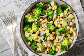 hearty, balanced salad of broccoli, chickpeas, avocado, onion, and parsley with a lemon oil dressing, close-up in a bowl on the table. Horizontal top view from above