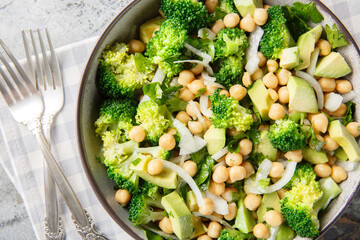 green salad of broccoli, chickpeas, avocado, onion, and parsley with lemon oil, close-up in a bowl on a table. Horizontal top view from above