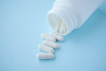 medicine pills capsule spilling out of bottle on blue background