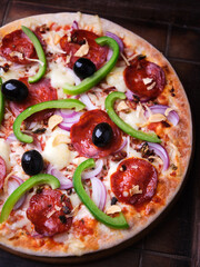 Pizza with chorizo ​​sausage, mozzarella cheese, green pepper and black olives. Rustic wooden background. Soft focus.	