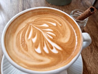 Hot cup of cappuccino with latte art on wooden table in cozy cafe