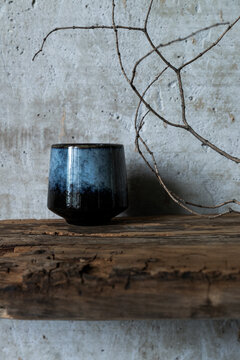 Dark ceramic cup on rustic wood with dry branch against concrete wall, minimal wabi sabi still life with natural textures.