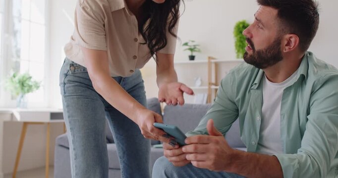 Couple fight over suspicions of infidelity and cheating. Confrontation between jealous woman and man over messages on smartphone, wife arguing, grabbing phone from husbands hand, showing jealousy