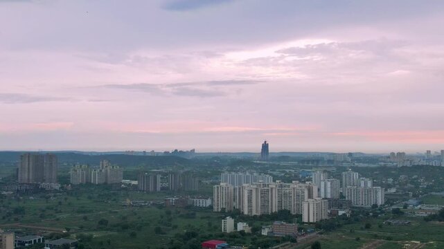 aerial drone shot moving sideways over cityscape with multi-storey buildings in the middle of green fields under the pink cloudy monsoon sky in Indore, Jaipur, Kolkata, Gurugram