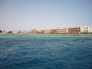 Hurghada, Egypt – 2010: Palm trees and low, resort-style buildings line a narrow strip of land surrounded by the turquoise and deep blue waters of the Red Sea, with a clear, sunny sky overhead and a