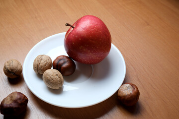 Ripe red apple resting on a white plate with assorted nuts