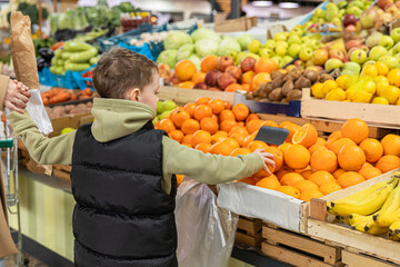 Little boy and his mom buy tangerines, oranges and green apples at farmer's market. Healthy nutrition concept. High quality photo