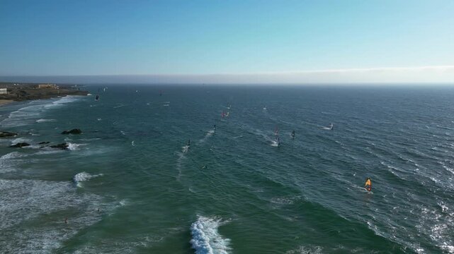 Panoramic drone shot of kite surfers, surfing in waves of sunny Guincho, Portugal