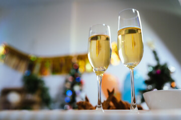 Two glasses of champagne on a festive table with blurred Christmas decorations and warm holiday lights in the background, symbolizing celebration and joy.