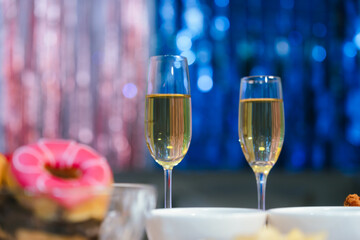 Two glasses of champagne on a festive table with blurred Christmas decorations and warm holiday lights in the background, symbolizing celebration and joy.