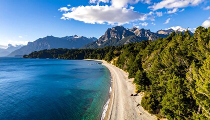 An aerial shot of a serene, turquoise lake meeting a rocky shoreline lined with trees, with mountains in the distance under a partly cloudy sky