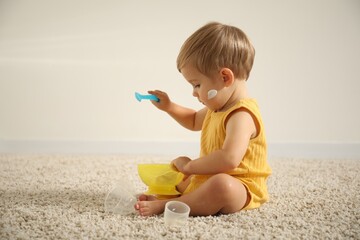 Cute baby with cream on his body playing at home. Space for text
