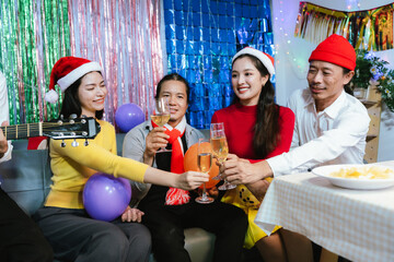Group of friends celebrating Christmas together, wearing festive hats, enjoying food and drinks, smiling and toasting with champagne at a joyful holiday party.