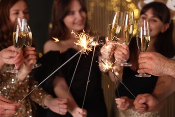 Friends celebrating New Year with sparklers and wine glasses indoors, selective focus