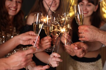 Friends celebrating New Year with sparklers and wine glasses indoors, selective focus