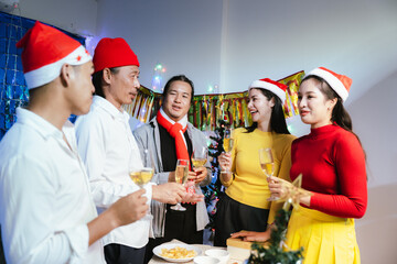 Group of friends celebrating Christmas together, wearing festive hats, enjoying food and drinks, smiling and toasting with champagne at a joyful holiday party.