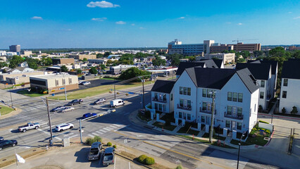 Cooper and Main Street intersection in downtown Arlington, Texas during peak hour. New development townhomes, retail buildings, and parking lots form a dense, transit-integrated urban corridor