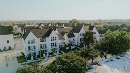 Three story white townhomes with balconies, dark roofs near college campus in downtown Arlington, TX. Rooftop HVAC units, adjacent commercial buildings, parking lots reflect mixed-use planning
