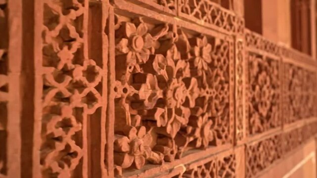 Ornate reddishbrown wall with intricate floral  geometric carvings receding into the distance