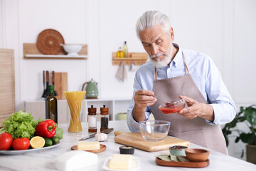 Elderly man cooking at white marble table in kitchen