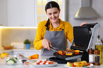 Woman cooking vegetables and meat on electric grill in kitchen