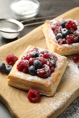 Tasty puff pastries with berries and powdered sugar on grey table, closeup