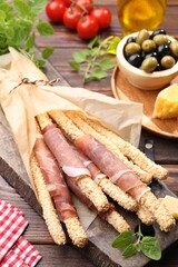Grissini breadsticks with prosciutto, olives and tomatoes on wooden table, closeup