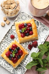 Tasty puff pastries with berries, mint, brown sugar and coffee on light grey table, flat lay