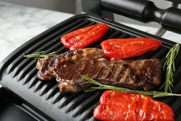 Electric grill with beef steaks, bell peppers and rosemary on white marble table, closeup