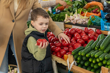 Side view unrecognizable mom and little boy son buying fresh cucumbers and tomatoes at farmer's market. Healthy nutrition concept. High quality photo