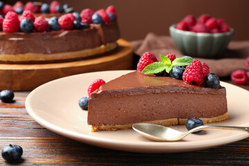 Piece of tasty chocolate cheesecake with berries on wooden table, closeup