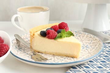 Piece of delicious cheesecake with fresh berries and mint served on white table, closeup