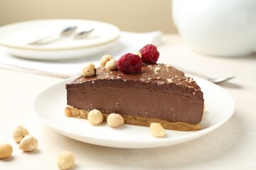 Piece of delicious chocolate cheesecake with nuts and raspberries on beige table, closeup