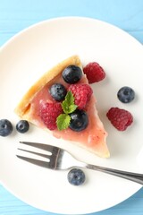 Piece of tasty cheesecake with berries and sauce on light blue wooden table, top view
