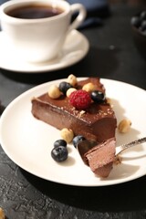 Piece of delicious chocolate cheesecake with nuts, berries and tea on black table, closeup