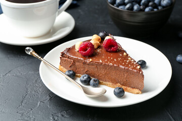 Piece of delicious chocolate cheesecake with nuts, berries and tea on black table, closeup