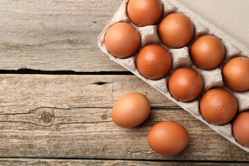 Raw chicken eggs in egg carton on wooden table, top view. Space for text