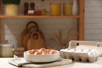 Raw chicken eggs in bowl and carton on white table in kitchen. Space for text