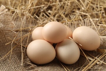 Raw chicken eggs and straw on table, closeup