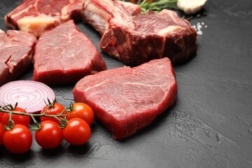 Pieces of raw beef meat, spices and tomatoes on black table, closeup. Space for text