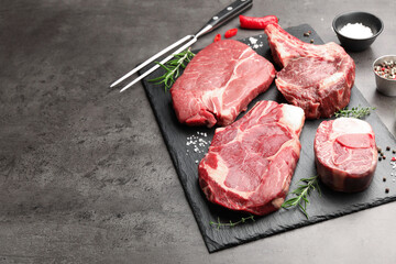 Pieces of raw beef meat, spices and carving fork on grey table, closeup. Space for text