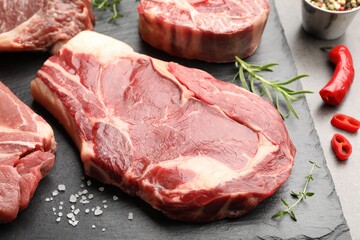 Pieces of raw beef meat and spices on grey table, closeup