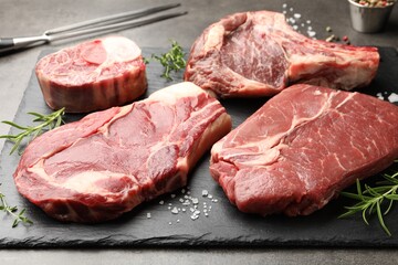 Pieces of raw beef meat, spices and carving fork on grey table, closeup