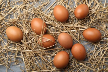 Raw chicken eggs and straw on grey wooden table, flat lay