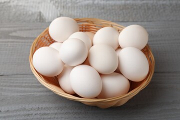 Raw chicken eggs in wicker basket on grey wooden table, closeup