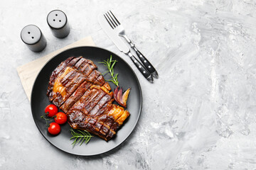 Delicious grilled beef steak with rosemary, onion, tomatoes, cutlery and shakers on grey textured table, flat lay. Space for text