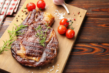 Delicious grilled beef steak with herbs, spices and tomatoes on wooden table, closeup. Space for text