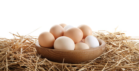 Raw chicken eggs in bowl on straw against white background