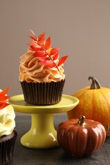 Delicious cupcakes with branches with red leaves and decorative pumpkins on grey textured table, closeup. Autumn atmosphere